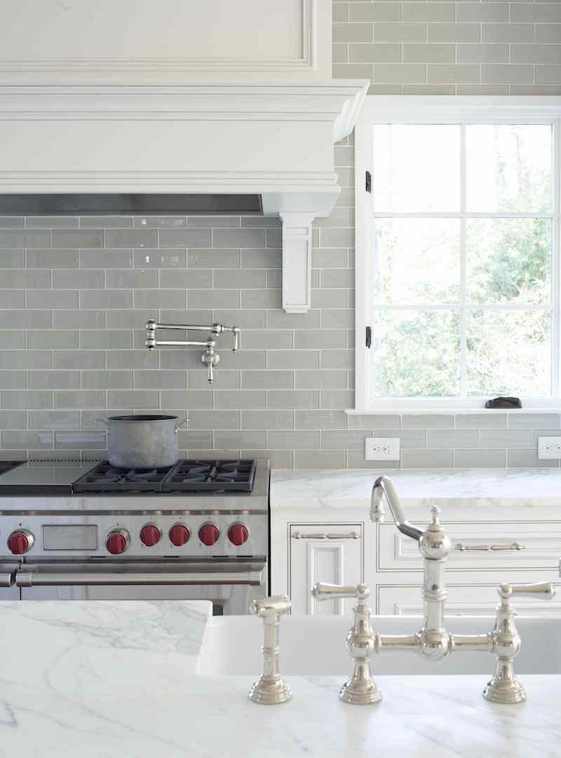 gray glass kitchen backsplash with carrera marble counters in a pretty traditional white kitchen. Nickel faucet and wolf range